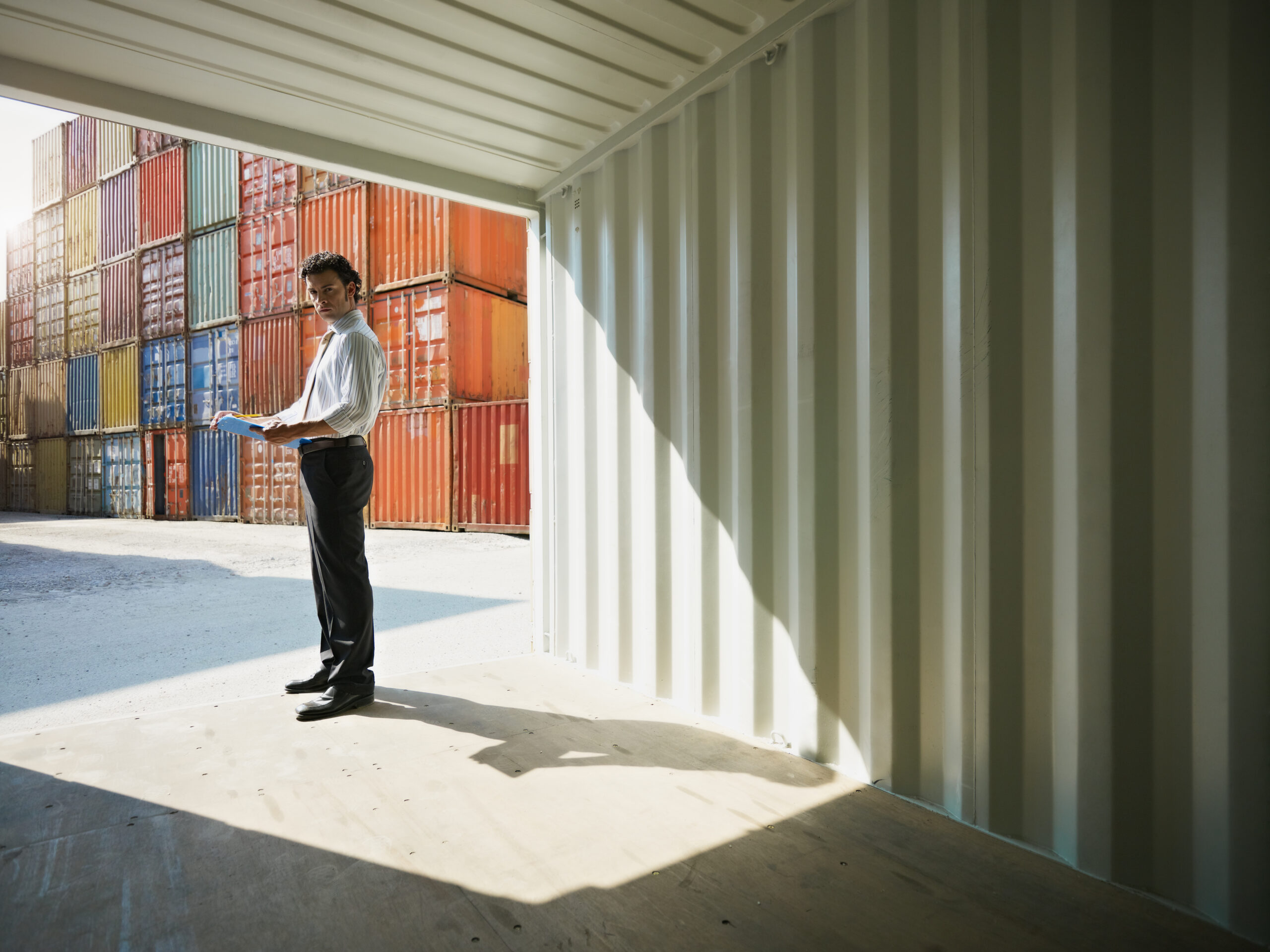 portrait of mid adult businessman standing inside cargo container and looking at camera. Horizontal shape, side view, copy space